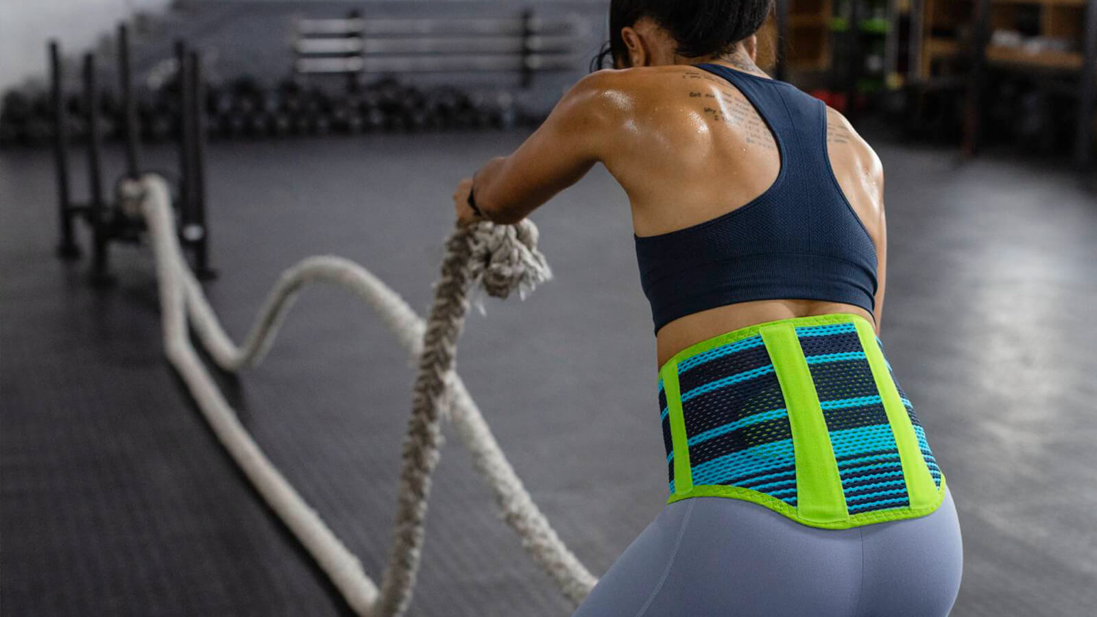 Woman wearing the Sports Back Support while performing a rope exercise inside a gym. Woman wearing Bauerfeind's Sports Back Support while performing a rope exercise in an indoor gym.