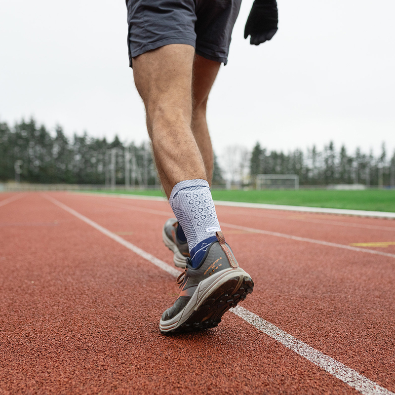 Male Athlete Training on Running Track - Sports and Fitness Focus Close-up of a male runner's legs wearing blue running shoes and compression socks on a red running track.