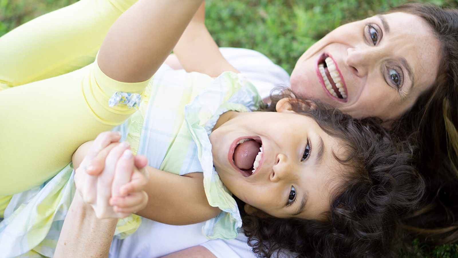 Mother and daughter playing and laughing together on grass. Mother and daughter playing and laughing together on grass, capturing a joyful moment outdoors.