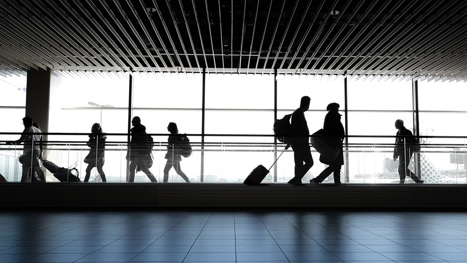 Airport travelers walking through the terminal. Silhouettes of people walking in an airport terminal with large windows and modern architecture, highlighting the hustle of travel.
