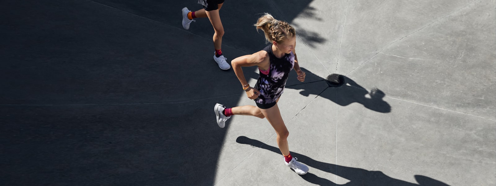 Two women running outside while wearing Bauerfeind's Sports Ankle Support. Two women running outside while wearing Bauerfeind's Sports Ankle Support.