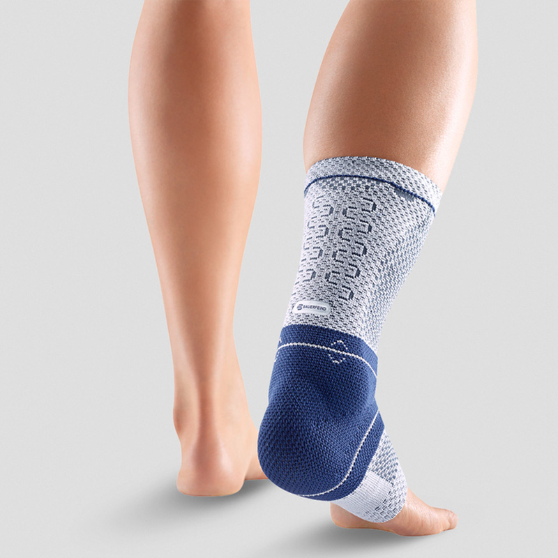 Close-up view of a person wearing a blue and white ankle support brace demonstrating its fit and design on a neutral background