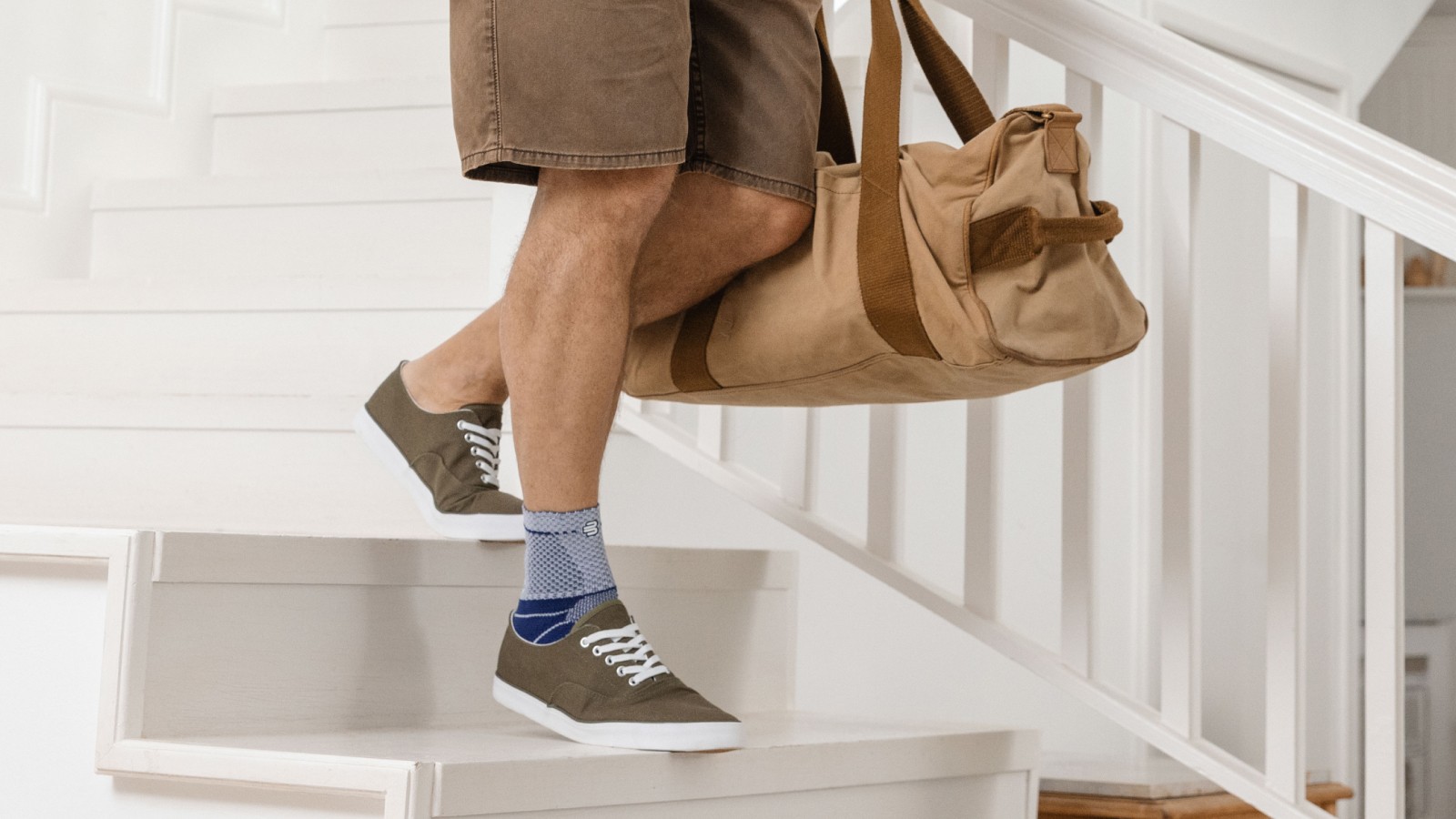 Man wearing Bauerfeind's MalleoTrain ankle brace while walking down steps holding a travel bag.