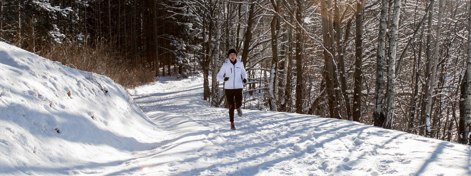 Woman running uphill while wearing the Run Performance Compression Socks. Woman running uphill through snowy weather while wearing cold weather gear and Bauerfeind's Run Performance Compression Socks.