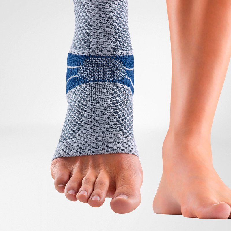 Close-up of a gray and blue ankle support brace on a person's left foot, showing detailed fabric texture and supportive bands, isolated on a white background.