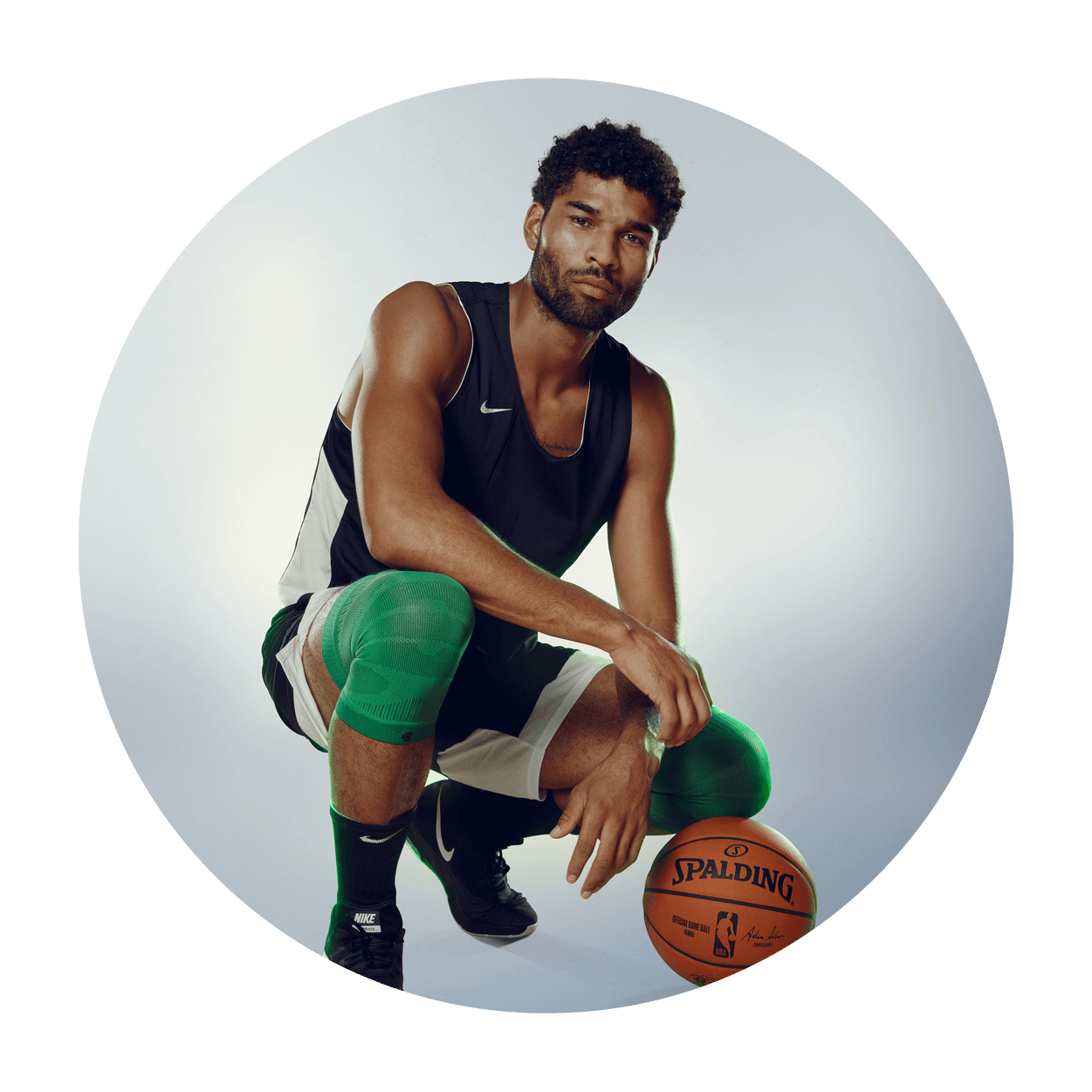 Athlete bending down near a basketball while wearing the Sports Compression Knee Support NBA Celtics Edition. Athlete bending down near a basketball while wearing Bauerfeind's Sports Compression Knee Support NBA Celtics Edition.