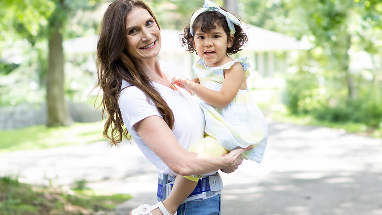 Smiling mother holding her child while wearing the SacroLoc. Smiling mother holding her child while wearing Bauerfeind's SacroLoc SI joint belt.