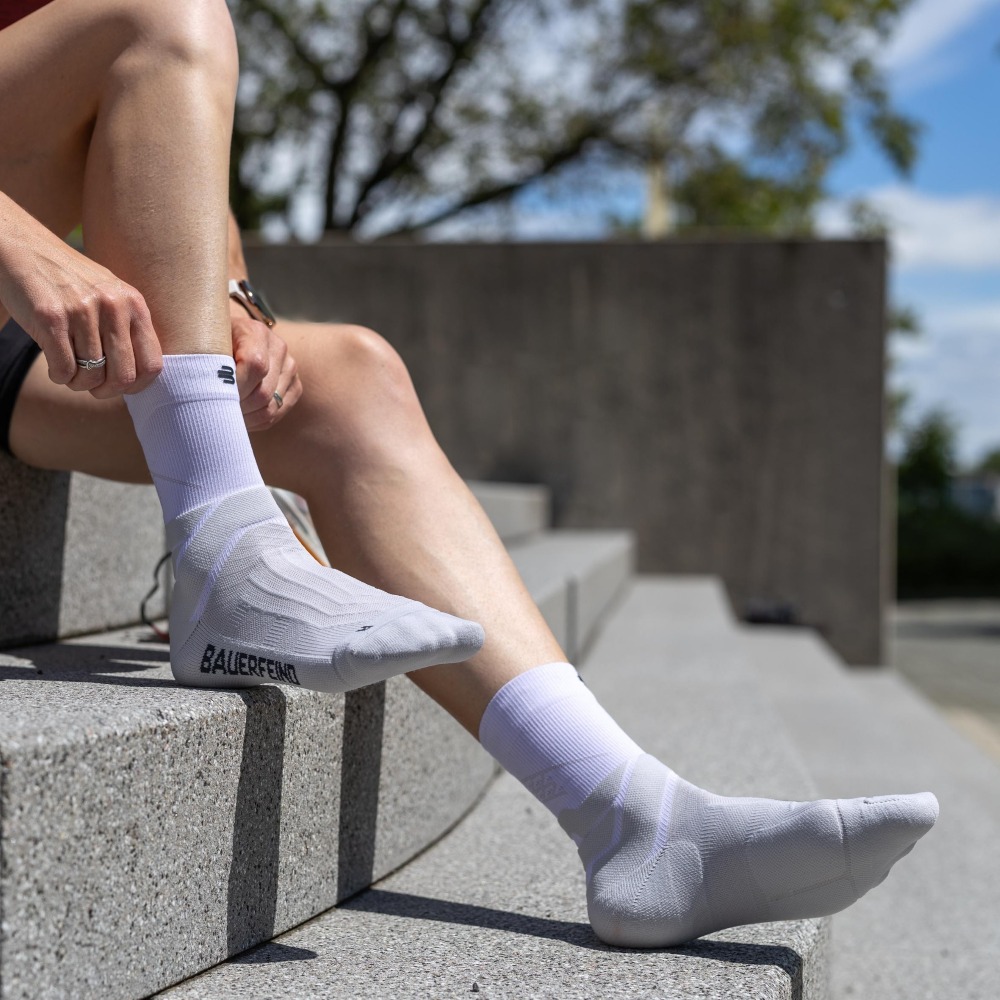 Athlete putting on the white Run Performance Mid-Cut Socks while sitting on concrete steps.