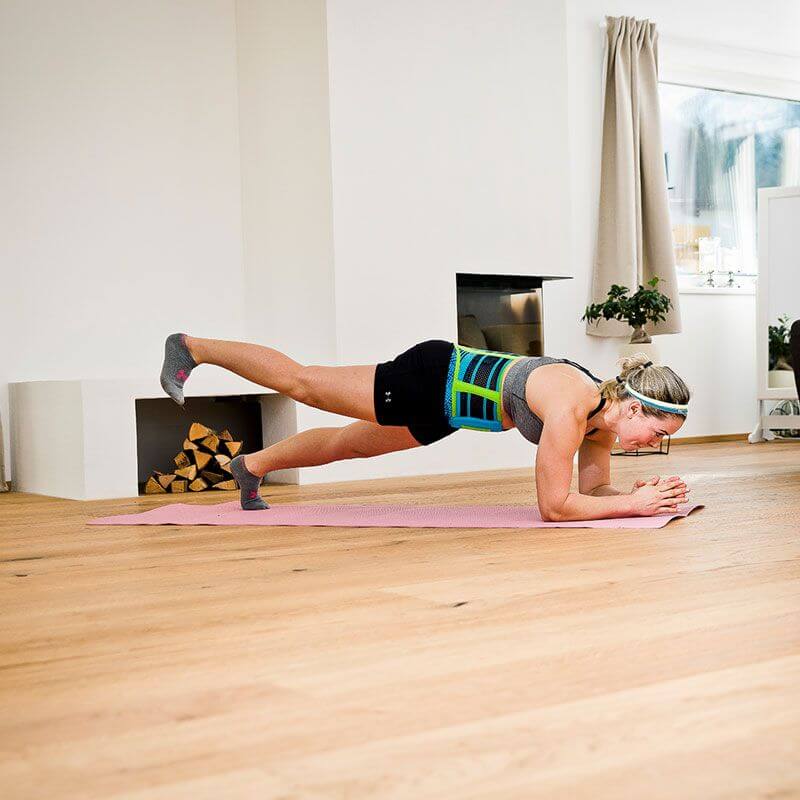 Woman performing the plank exercise while wearing the Sports Back Support. Woman performing the plank exercise while at home wearing Bauerfeind's Sports Back Support.