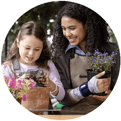 Woman planting flowers with a child while wearing the ManuTrain. Woman planting flowers with a child while wearing Bauerfeind's ManuTrain wrist brace.