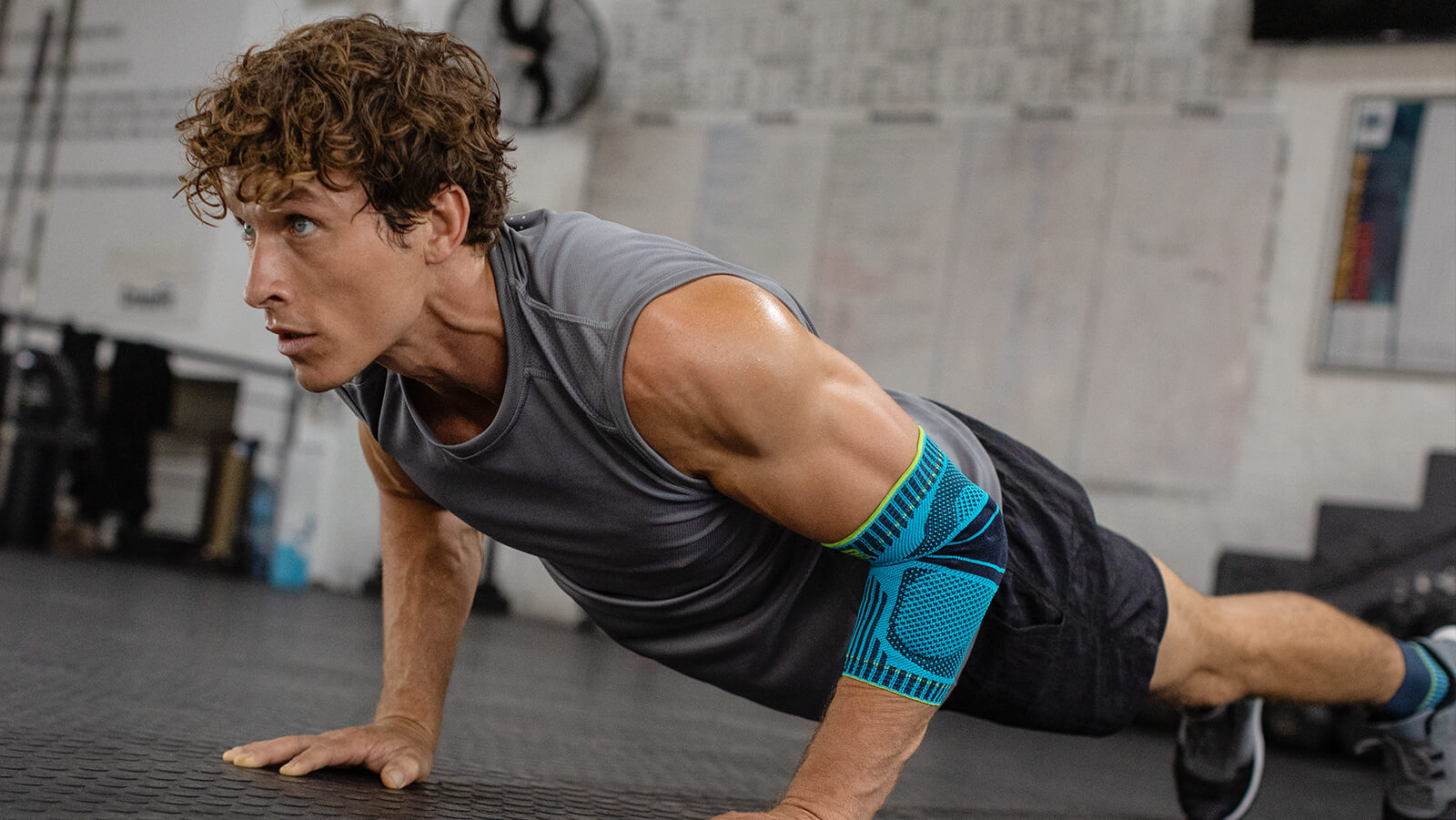 Man performing push-ups in the gym while wearing the Sports Elbow Support. Man performing push-ups in the gym while wearing Bauerfeind's Sports Elbow Support.