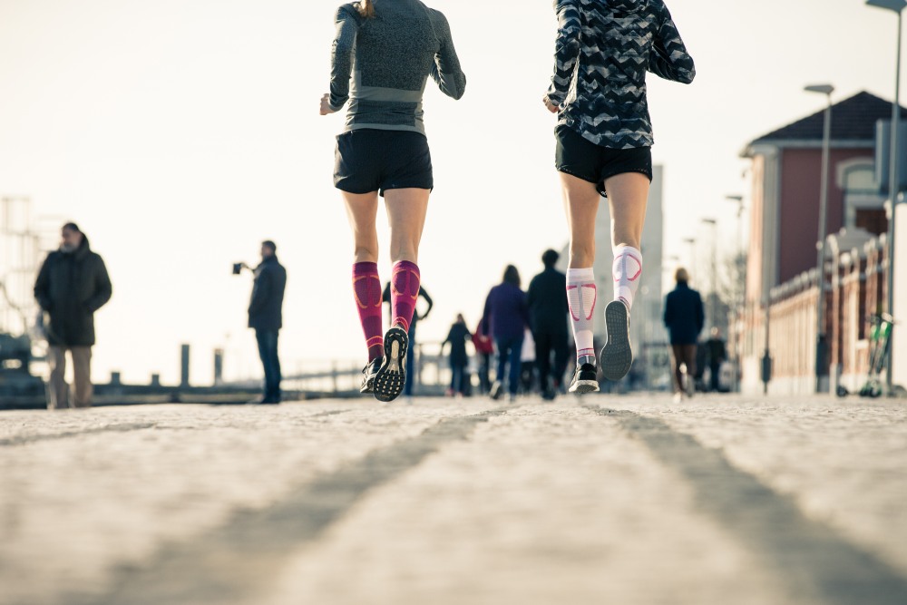 Woman wearing the Run Performance Compression Socks while running through a city street. Woman wearing Bauerfeind's Run Performance Compression Socks while running through a city street.
