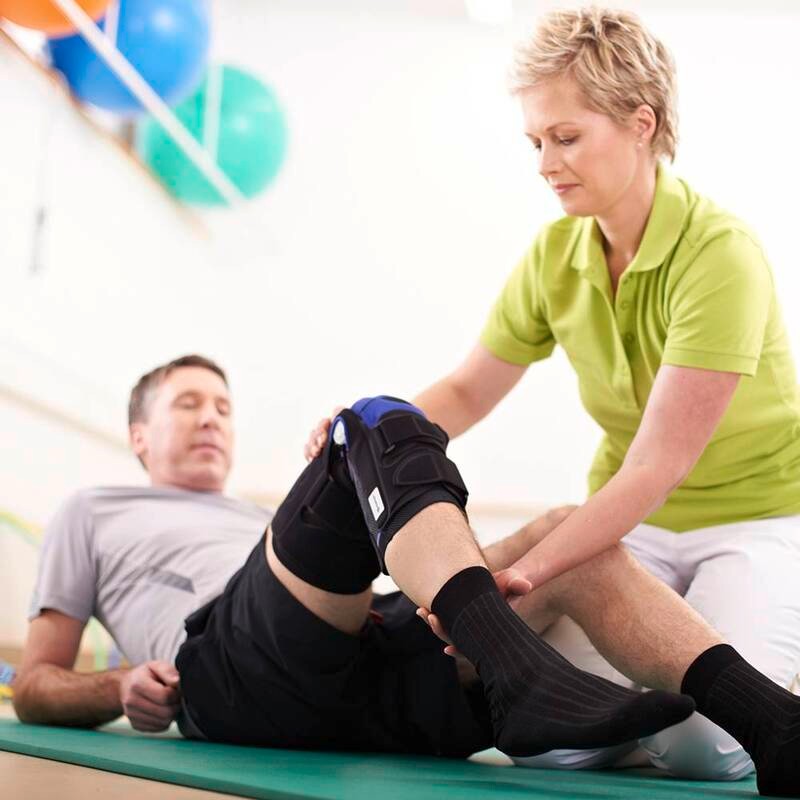 Physical therapist assisting a male patient with knee brace adjustment in clinic