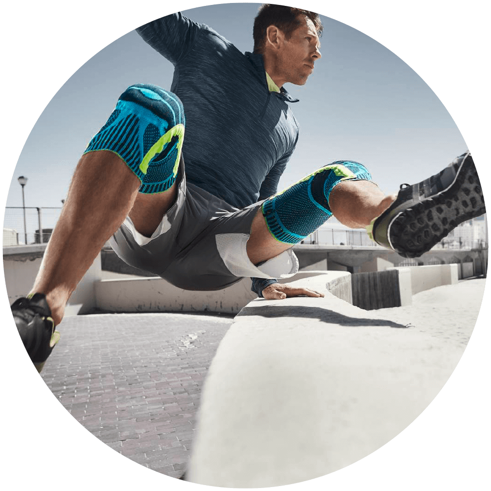 Made for Athletes Man jumping over a concrete wall while wearing Bauerfeind's Sports Knee Support.
