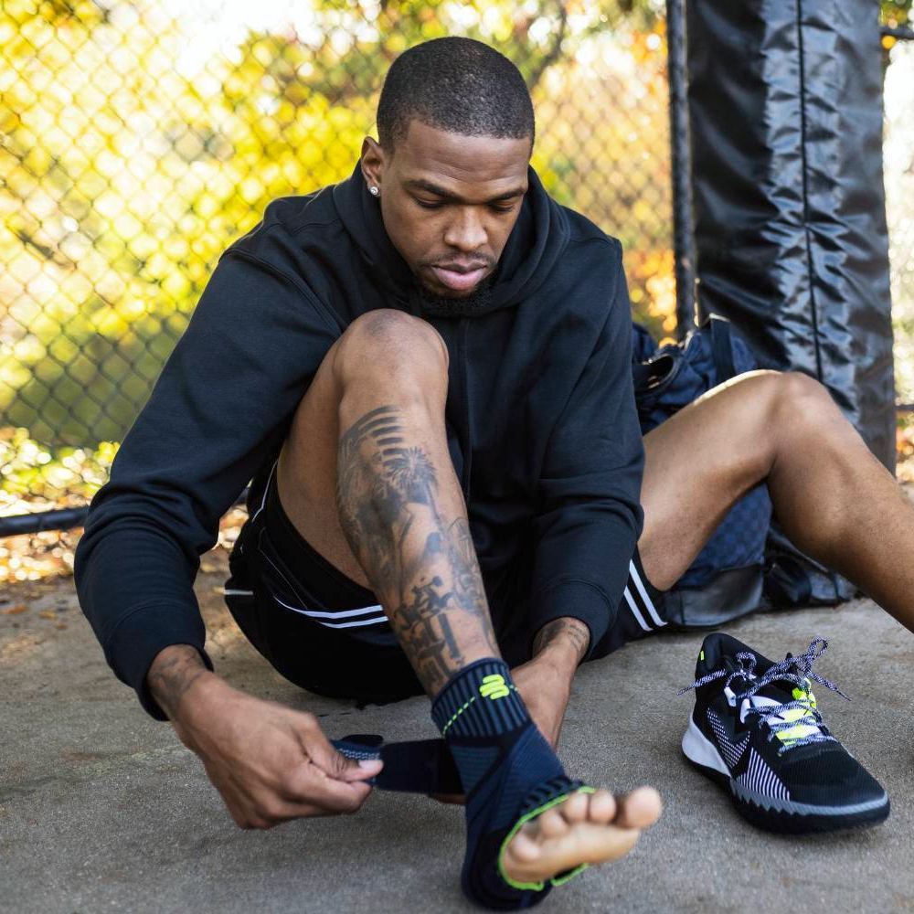 Basketball player sitting on a basketball court and takes on a black ankle support