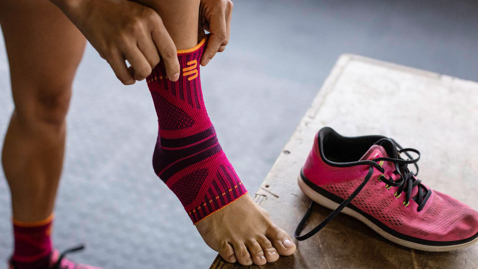Woman donning the Sports Ankle Support Dynamic before exercising. Woman donning Bauerfeind's Sports Ankle Support Dynamic before working out in a fitness center.