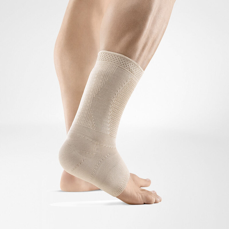 Close-up view of a beige ankle support brace on a human leg against a light grey background, highlighting the snug fit and breathable fabric of the medical gear.