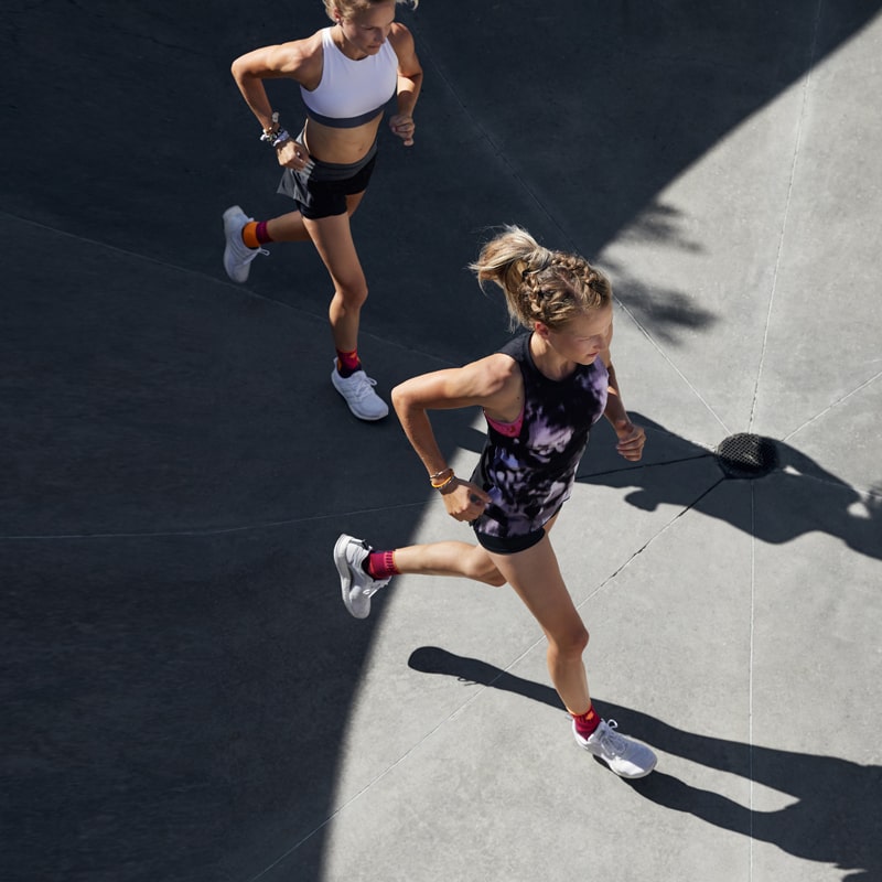 Two women running outside while wearing Bauerfeind's Sports Ankle Support. Two women running outside while wearing Bauerfeind's Sports Ankle Support.