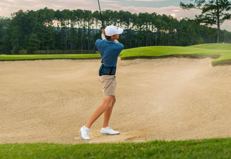 Golfer wearing Bauerfeind's Sports Back Support while hitting out of a sand bunker.