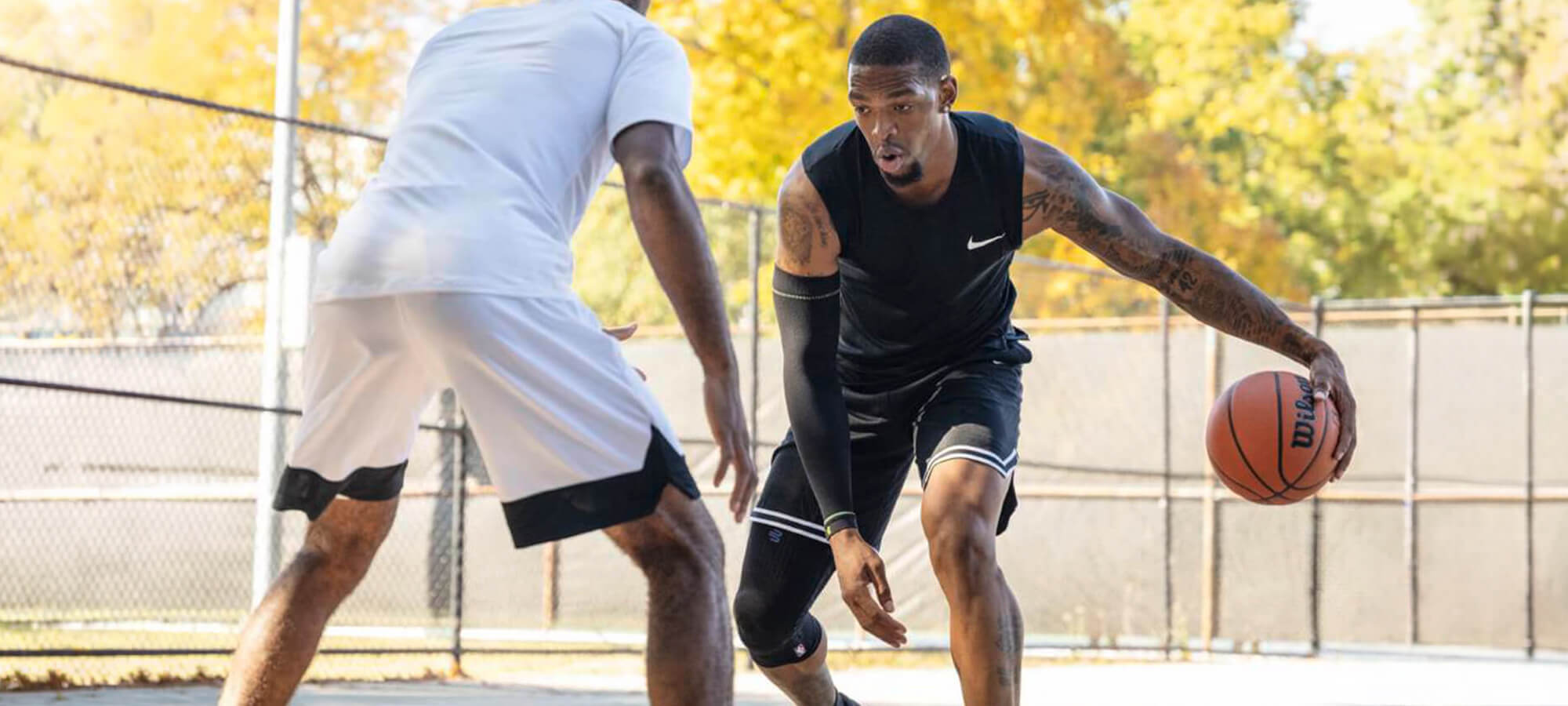 Basketball player defending another basketball player who's wearing Bauerfeind's Sports Compression Knee Support NBA in an indoor court.