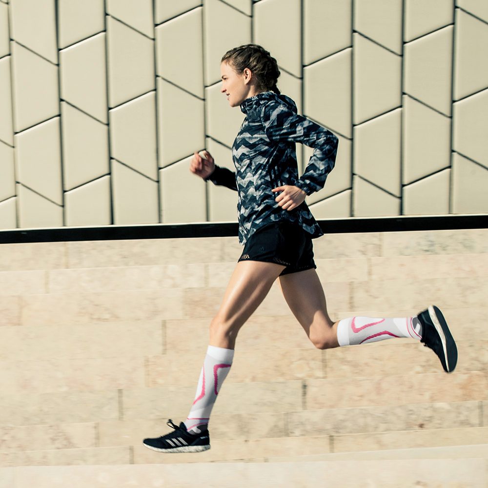 Woman wearing the Run Performance Compression Socks while running through a city street. Woman wearing Bauerfeind's Run Performance Compression Socks while running through a city street.