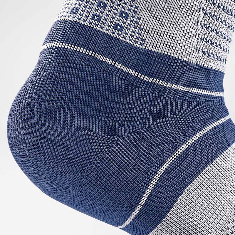 Close-up view of a person wearing a blue compression ankle brace on their left foot, set against a plain light gray background.