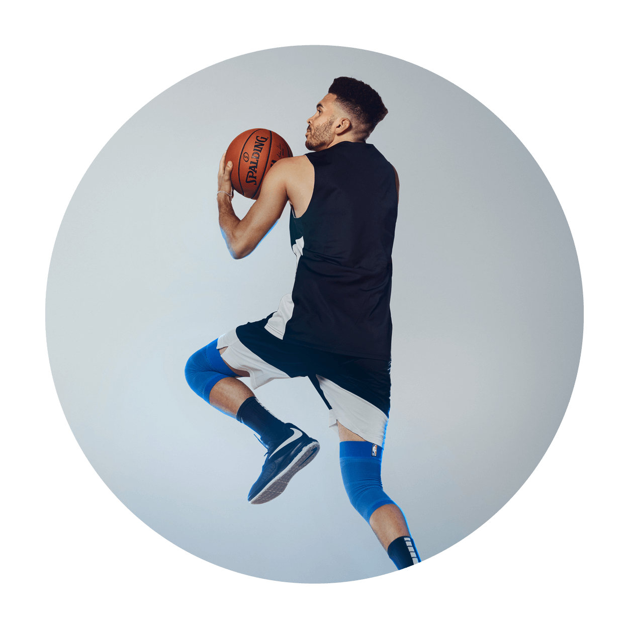 Athlete attempting a layup while wearing the Sports Compression Knee Support NBA Mavericks Edition. Athlete attempting a layup on an indoor basketball court while wearing Bauerfeind's Sports Compression Knee Support NBA Mavericks Edition.