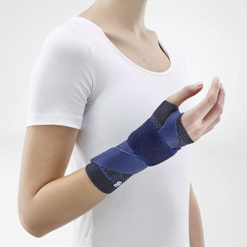 Woman Wearing the ManuTrain (Black) Woman wearing Bauerfeind's ManuTrain wrist brace (black) while standing in front of a gray background.