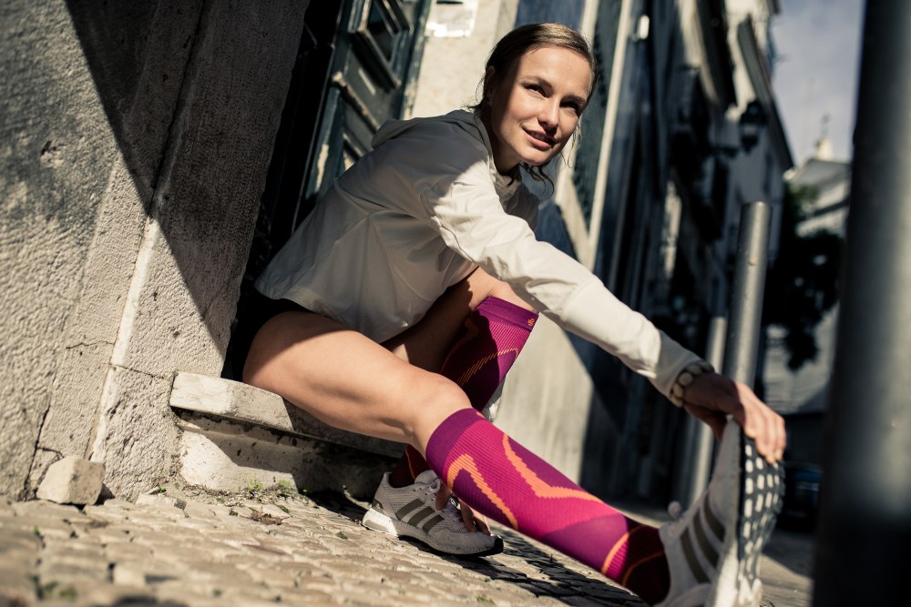 Young woman stretching while wearing the Run Performance Compression Socks before an inner-city run. Young woman stretching while wearing Bauerfeind's Run Performance Compression Socks before an inner-city run.