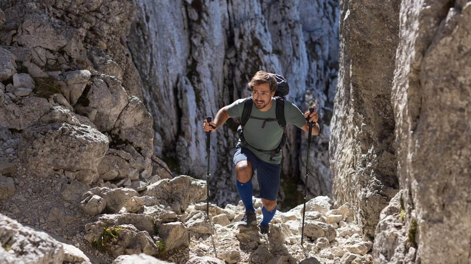 Outdoor Merino Compression Socks While Hiking Man wearing Bauerfeind's Outdoor Merino Compression Socks while hiking through rocky mountain terrain using trekking poles.