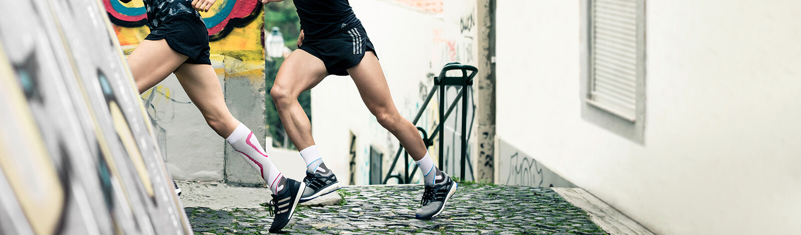 Two young adults wearing the Run Performance Compression Socks while running uphill. Two young adults wearing Bauerfeind's Run Performance Compression Socks while running uphill in an inner-city street.