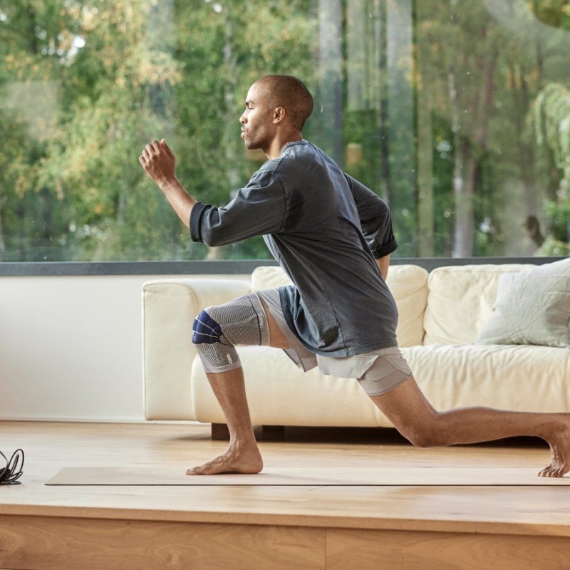 Man performing lunges during an in-home workout while wearing the GenuTrain. Man performing lunges during an in-home workout while wearing Bauerfeind's GenuTrain knee brace.
