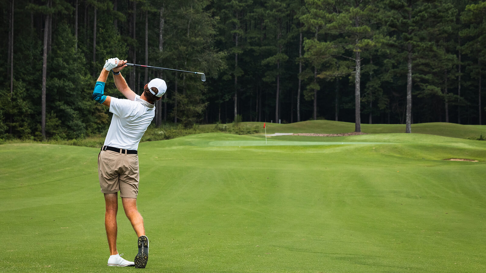 Golfer wearing Bauerfeind's Sports Elbow Support while hitting out of the fairway.