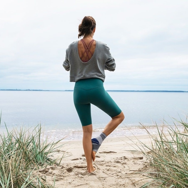 Woman practicing yoga near the ocean while wearing Bauerfeind's MalleoTrain S ankle brace.