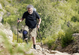 Senior man wearing Bauerfeind's GenuTrain OA unloader knee brace while hiking up a rocky mountain trail.