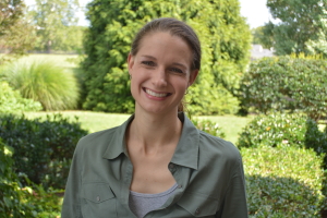 Ashley Eriksen smiling while standing in front of hedges and trees.