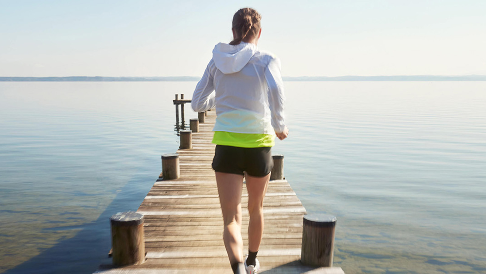 Morning jog on a lakeside pier. Woman running on a wooden pier over a calm lake.