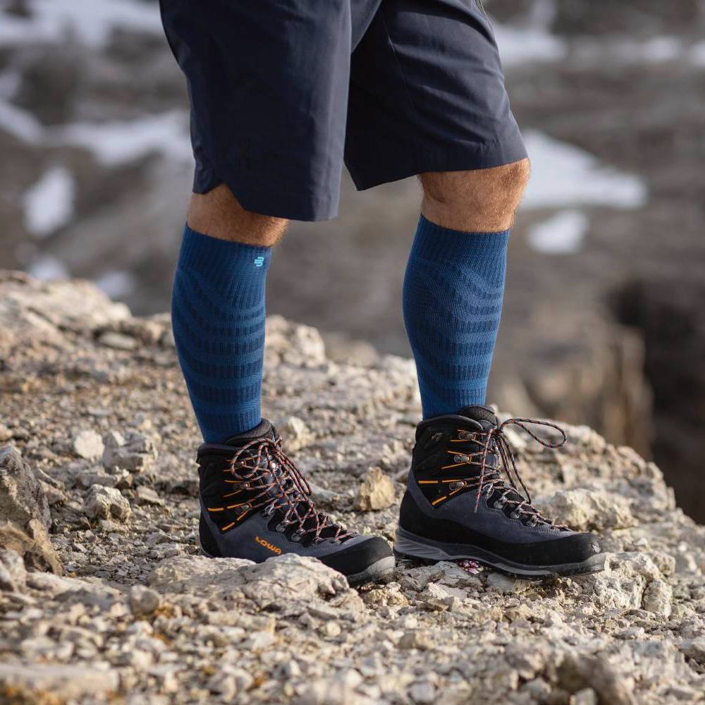 Hiker with Blue Compression Socks and Black Hiking Boots on Rocky Terrain Hiker wearing blue compression socks and black hiking boots standing on rocky terrain