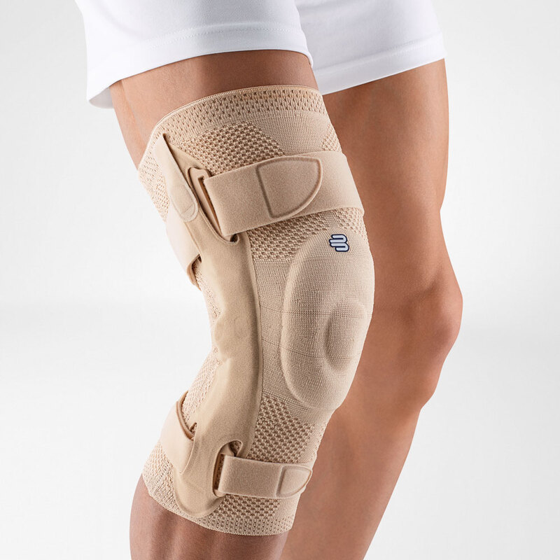 Close-up view of Bauerfeind's beige GenuTrain S hinged knee brace on a person's leg, showcasing adjustable straps and knee pad for joint stability and injury recovery.