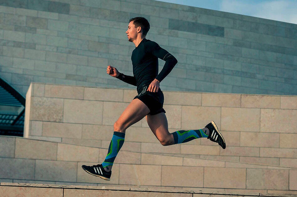 Young man wearing Bauerfeind's Run Performance Compression Socks while running on a concrete path inside of a city.
