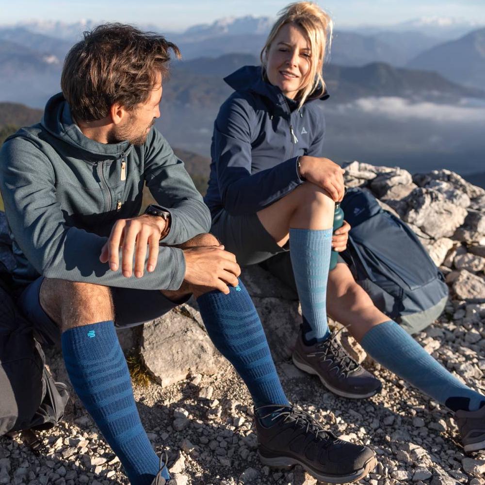 Hikers Resting in Outdoor Gear with Mountain View Hikers enjoying a mountain view while resting on rocky terrain, wearing blue and green outdoor gear and knee-high compression socks.