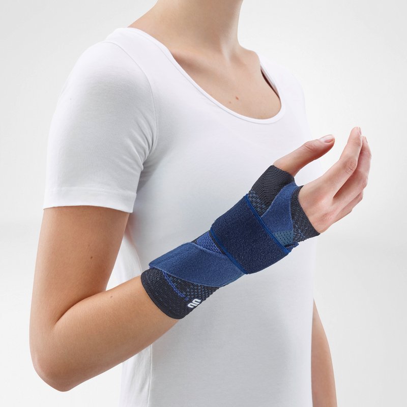 Woman wearing Bauerfeind's ManuTrain wrist brace (black) while standing in front of a gray background.
