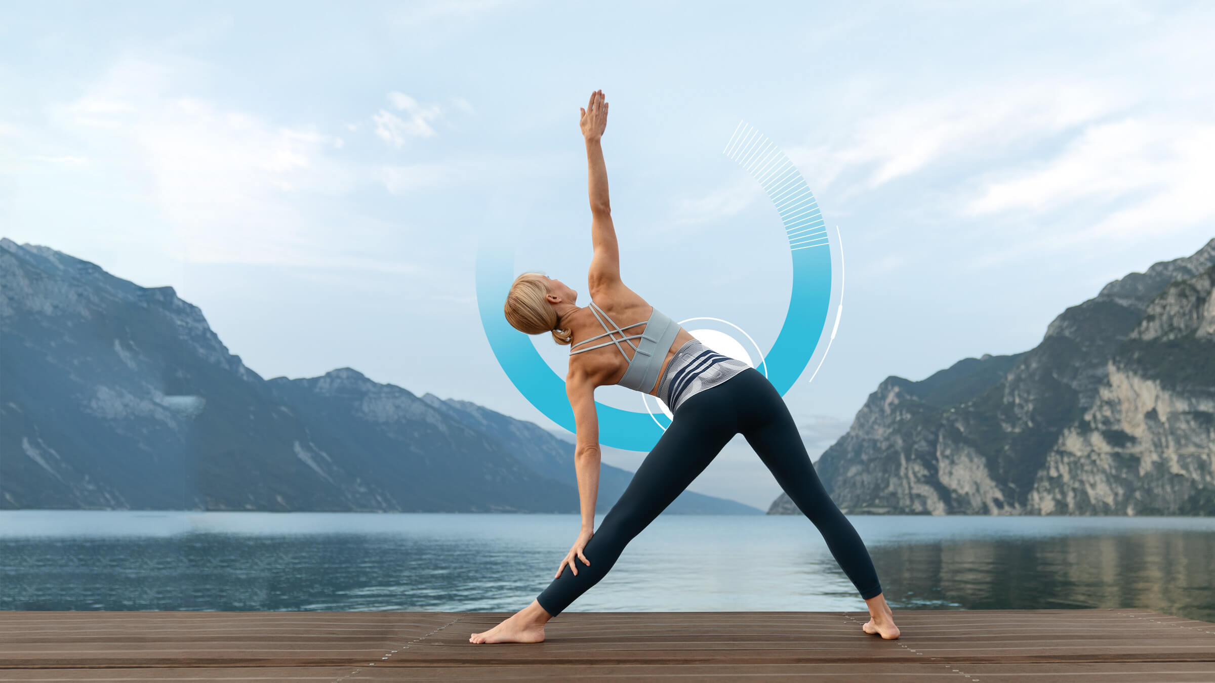 Woman wearing the LumboTrain (waisted) while practicing yoga outdoors. Woman wearing Bauerfeind's LumboTrain waisted back brace while practicing yoga on a dock in front of a lake and mountains.