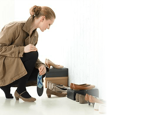 Woman bending down to select a shoe to insert her foot insole into. Woman bending down to select a shoe to insert her foot insole into.