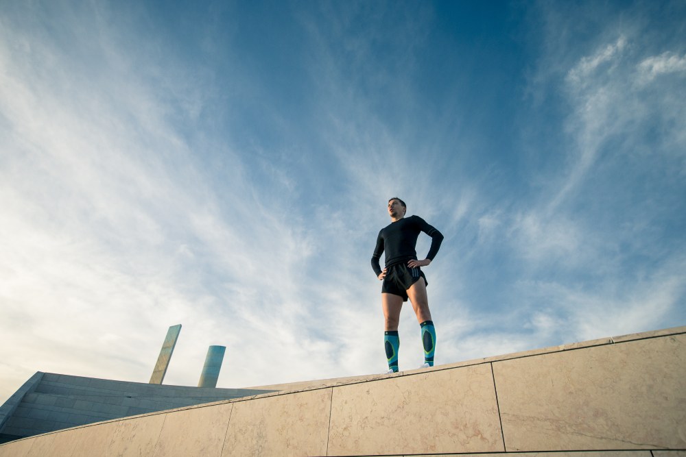 Man wearing Bauerfeind's Run Performance Compression Socks while resting on a concrete wall.