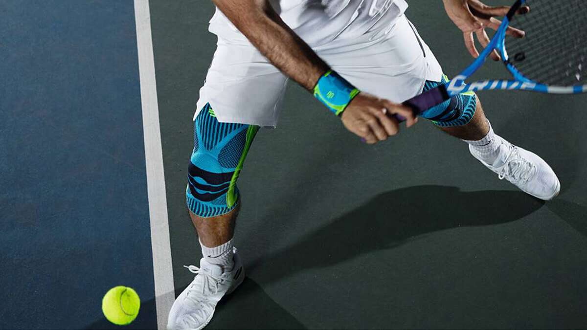 Tennis player wearing the Sports Knee Support and Sports Wrist Strap while attempting to hit the ball. Tennis player wearing Bauerfeind's Sports Knee Support and Sports Wrist Strap while attempting to hit the tennis ball.