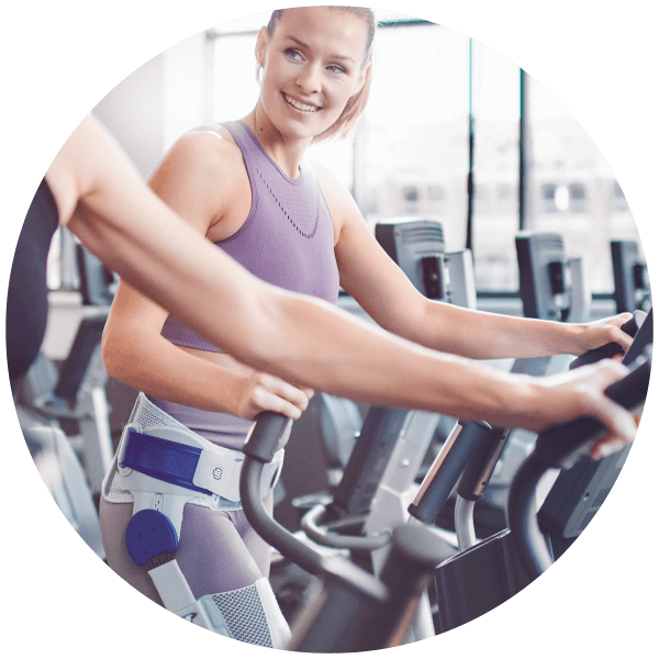 All-Day Comfort Woman using cardio machine during workout while wearing Bauerfeind's CoxaTrain hip brace.