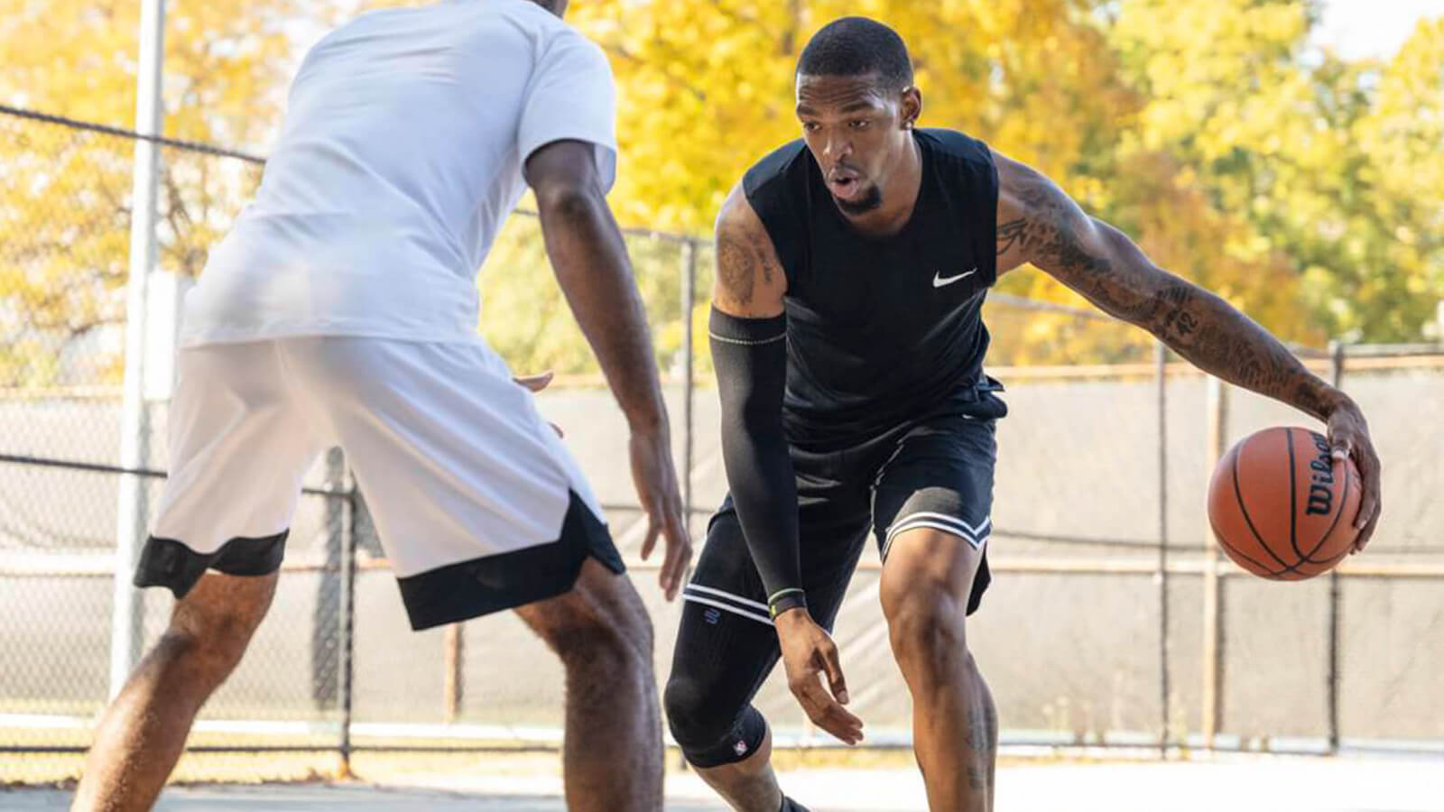 Trusted and Worn by the Pros Basketball player defending another basketball player who's wearing Bauerfeind's Sports Compression Knee Support NBA in an indoor court.