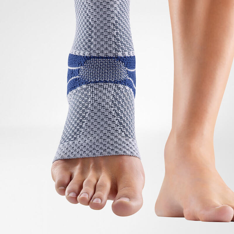 Ankle Support Brace for Injury Recovery and Protection Close-up of a gray and blue ankle support brace on a person's left foot, showing detailed fabric texture and supportive bands, isolated on a white background.