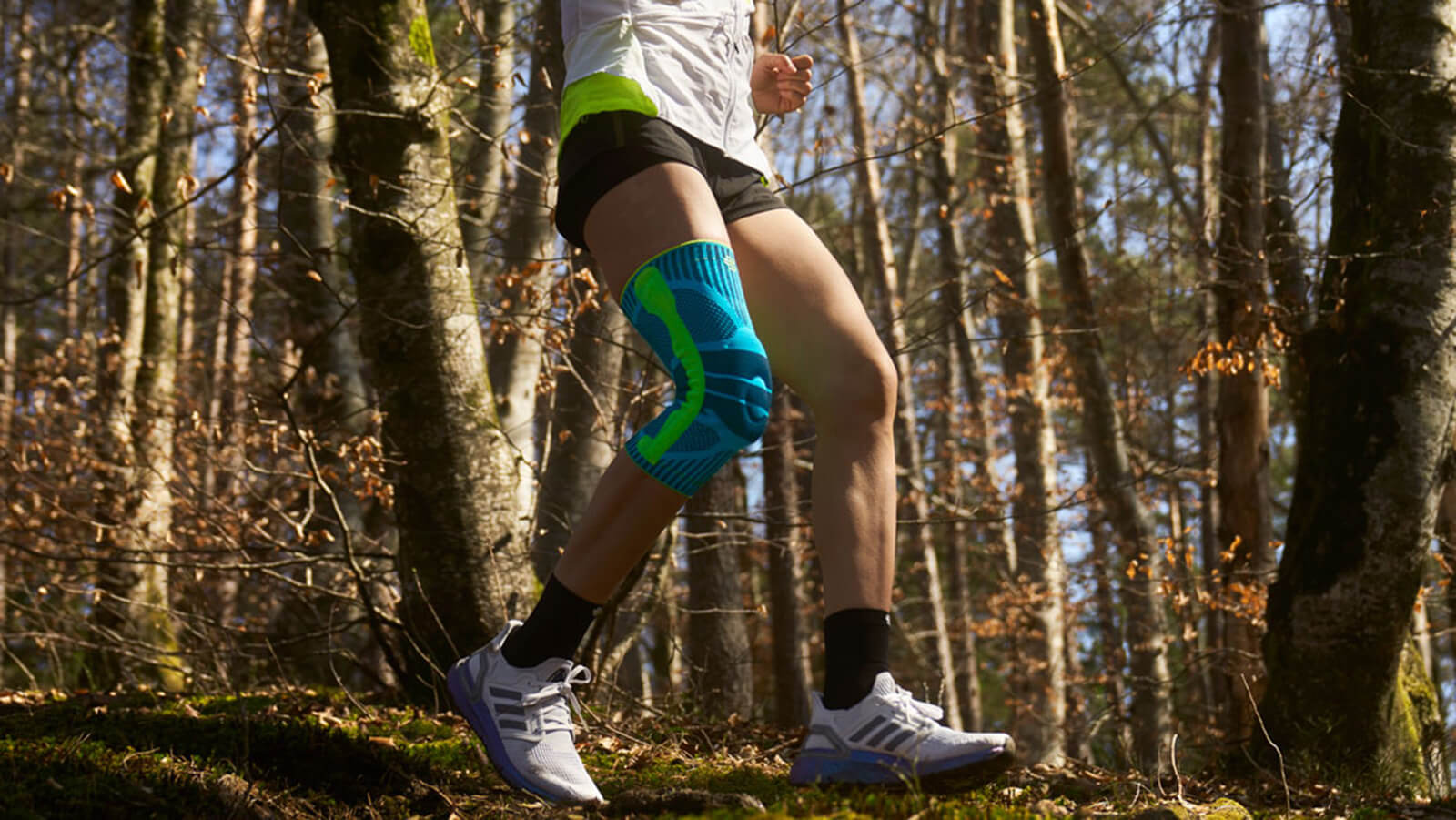 Best Knee Brace for Runners Woman wearing Bauerfeind's Sports Knee Support while running through a forest trail.